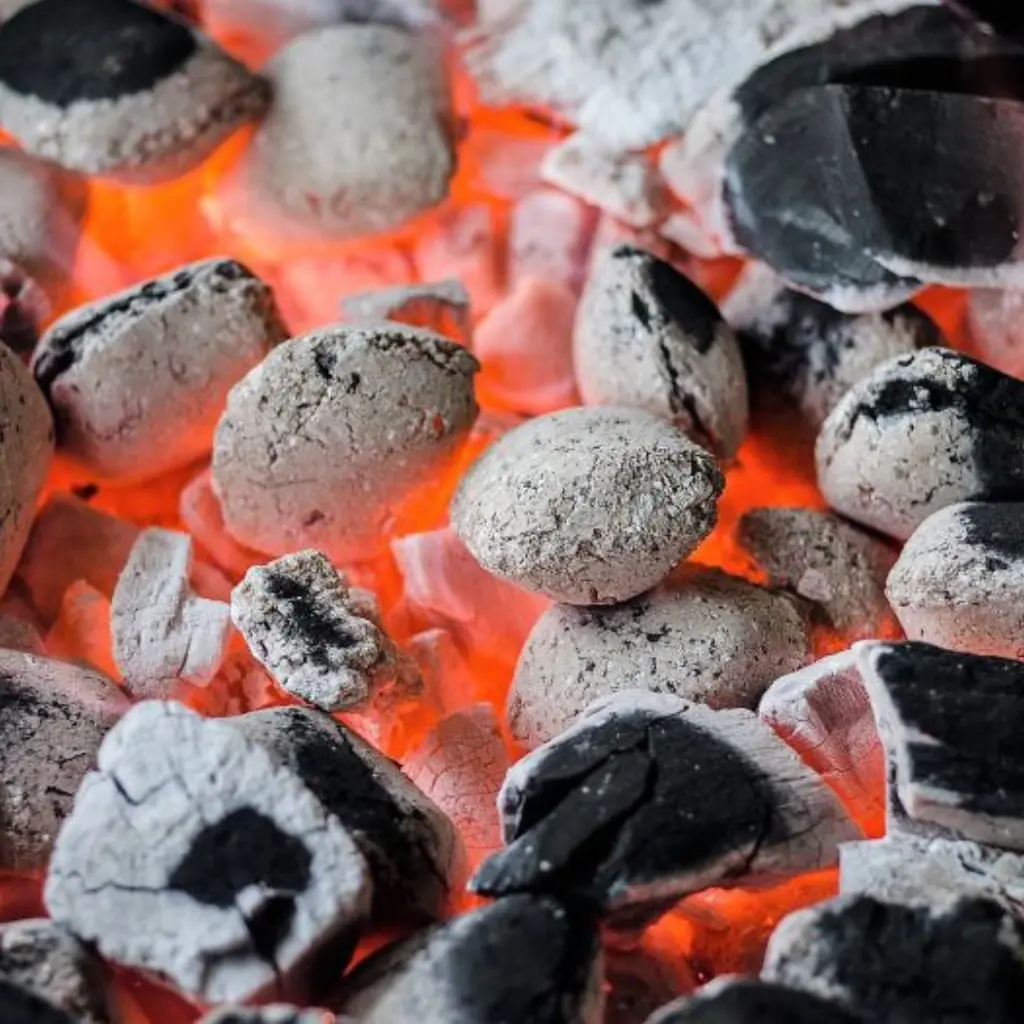 Brasas incandescentes cubiertas de ceniza que ilustran las propiedades del carbon como fuente de energía térmica y combustible